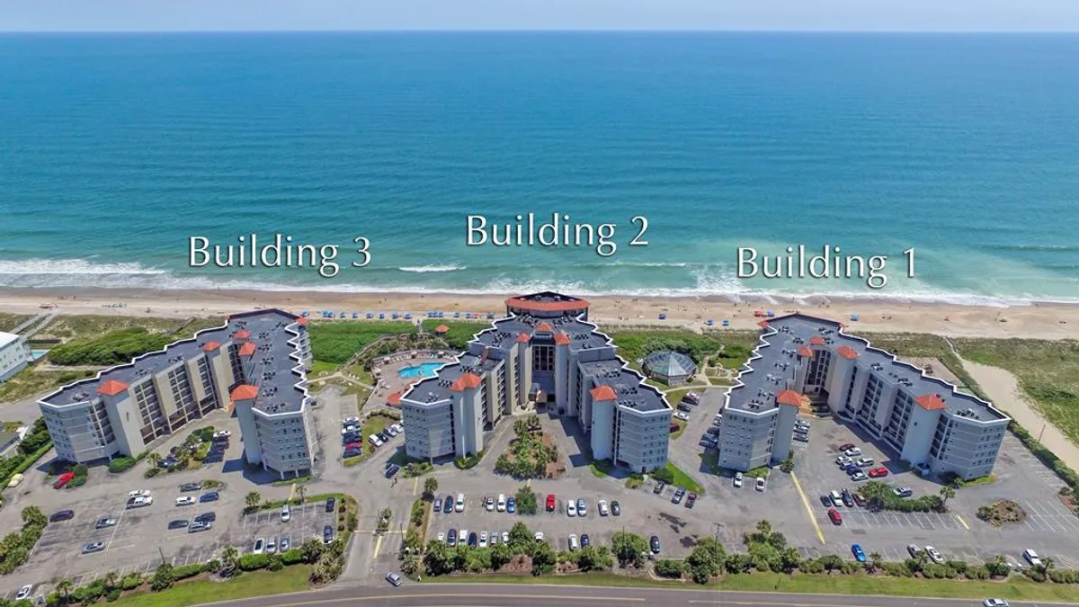 An exterior shot featuring a sparkling swimming pool surrounded by landscaped gardens, with the ocean and resort building in the background. The inviting pool area hints at leisurely swims, sunbathing, and sunset beach walks just steps away.