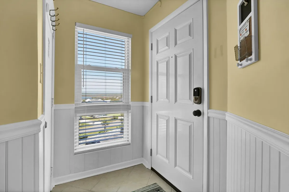 This image presents the entryway to the unit, featuring a front door, a window with blinds allowing natural light, and a decorative wall rack for organizing belongings. The overall mood is inviting, setting a welcoming tone upon arrival.