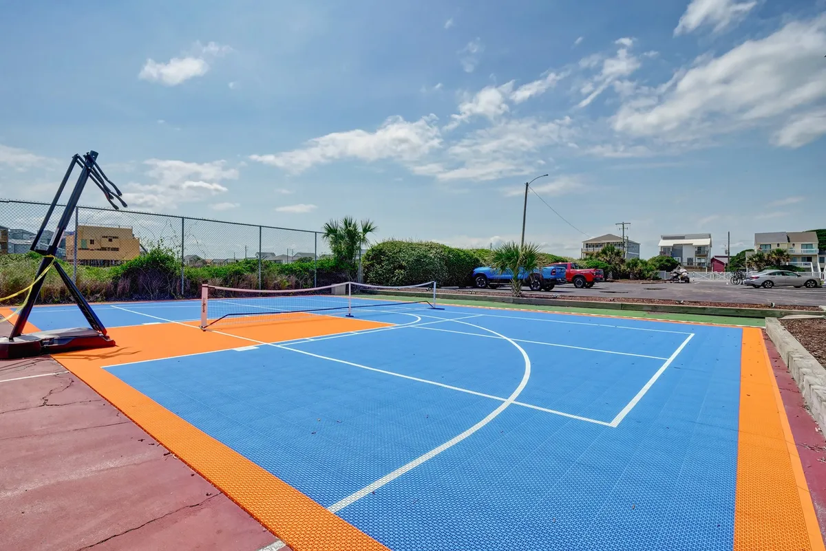 This exterior image displays a basketball court with a tennis net set amidst lush greenery. The space is designed for active recreation, inviting guests to participate in basketball or pickleball matches while enjoying the outdoors.