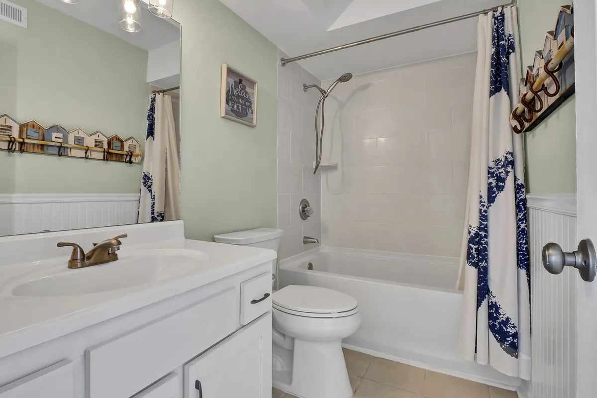 A calm, refreshing bathroom featuring a vanity with sink, decorative wall art, a shower/tub combo with a colorful curtain, and ambient lighting. The space is designed for relaxation and convenience, perfect for cleaning up after a day at the beach.