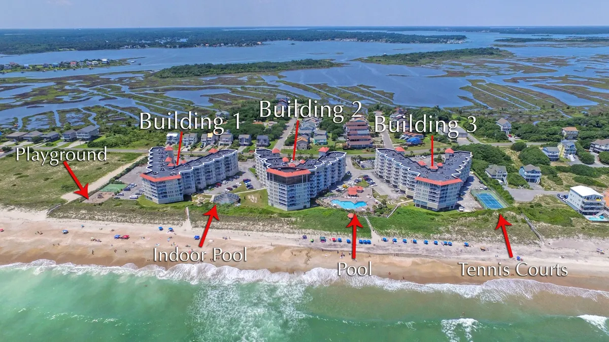 A sweeping exterior view of the resort complex displays both the indoor and outdoor pools, tennis courts, a vibrant playground area, and beachfront with families and children enjoying various activities. The red-roofed buildings, spacious pool decks, and activity zones are all visible, giving a lively, family-friendly impression.
