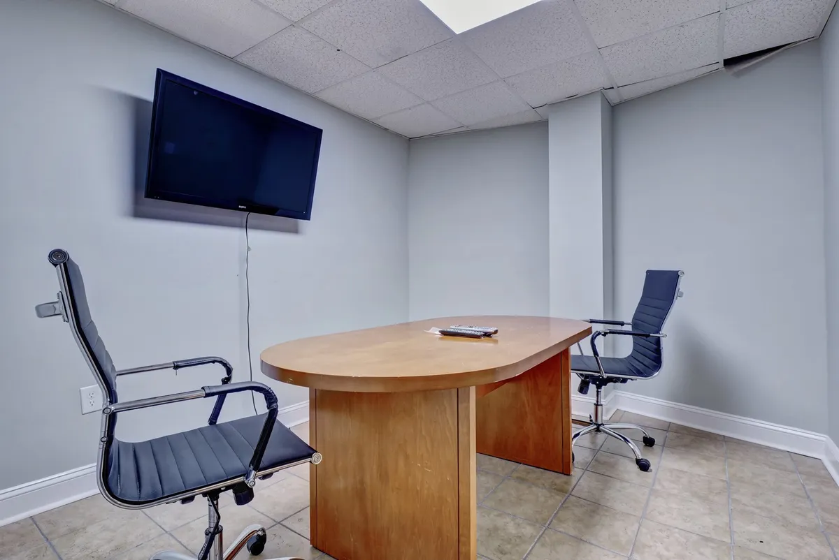 A modern business center setup with a wooden conference table, two office chairs, and a flat-screen TV, offering a private, productive environment for remote work or meetings.