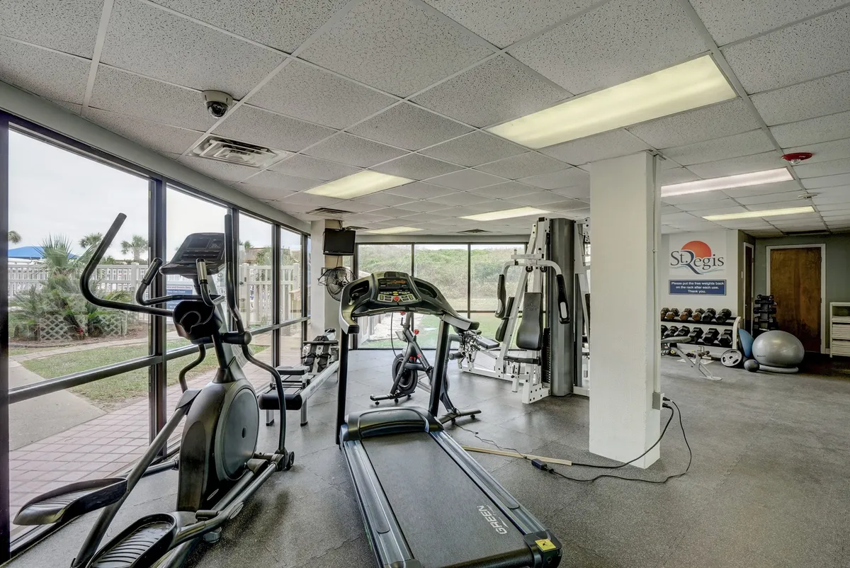 A spacious, modern fitness center featuring a treadmill, elliptical machine, weight equipment, and expansive windows letting in natural light. The setup encourages personal and group fitness activities in a motivating environment.