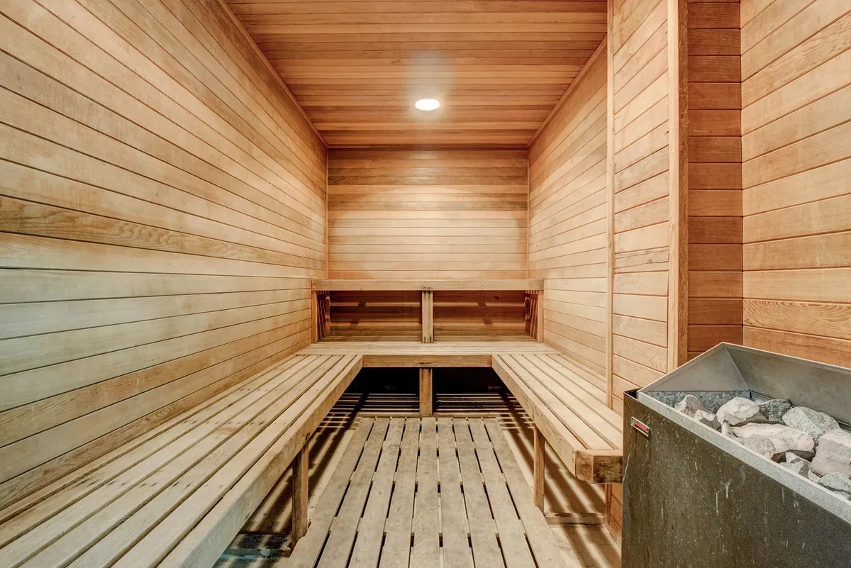 A beautiful sauna interior, with wooden benches and a stone heater, evoking a calming, spa-like feel. The warm wood tones and ambient light create a tranquil retreat for relaxation.