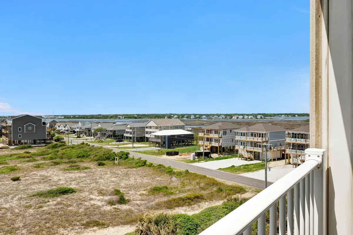A sweeping view from the condo’s balcony overlooking distant houses, open landscape, and a clear blue sky, conveying the relaxing and scenic coastal setting. The image hints at nearby outdoor spaces and the tranquility accessible just beyond the condo.